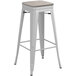 A white metal Lancaster Table & Seating barstool with a gray wooden seat.