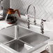 A stainless steel deck mount faucet with a 6-inch gooseneck spout and dual handles, installed on a kitchen sink.