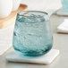 A blue Acopa stemless wine glass with ice water on a white coaster.