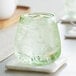 An Acopa green stemless wine glass filled with a clear liquid and ice on a white marble coaster.