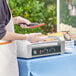 A person using a Carnival King hot dog roller to cook a hot dog.