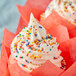 A cupcake with white frosting and Regal Rainbow Nonpareils on top.