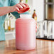 A woman pouring pink liquid into a Choice plastic container with a brown lid.