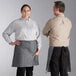 A man and woman wearing Acopa Kennett gray denim bistro aprons with black webbing.