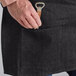 A person holding a bottle opener in the pocket of a black denim Acopa Kennett half bistro apron.