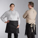 A man and woman wearing black Acopa Kennett half bistro aprons with natural webbing.