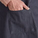 A man's hand in a pocket of a blue denim Acopa Kennett bib apron with black webbing.