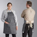 A man and woman standing at a counter, both wearing Acopa Kennett grey denim aprons.