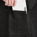 A person's hand putting a receipt in the pocket of a black Acopa bistro apron.