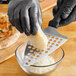 A person in black gloves grating cheese in a bowl with an American Metalcraft cheese grater.