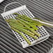 A stainless steel grill tray with asparagus cooking on a grill.