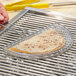 A hand using a yellow Outset grill basket to cook a quesadilla on a grill.