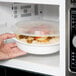A hand placing a Pactiv white round container of food in a microwave.