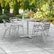 A Lancaster Table & Seating chrome square outdoor table with four silver arm chairs on a patio.