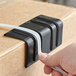 A person's hand holding a black box of PAC Strapping Products black plastic strapping edge protectors.