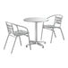 A Lancaster Table & Seating round chrome outdoor table with two silver arm chairs.