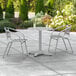 A Lancaster Table & Seating chrome round outdoor table and two chairs on a patio.