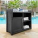 A black Mayne Fairfield outdoor towel valet cabinet with a door open and towels on top.