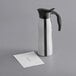 A silver stainless steel carafe with a black and white paper label.