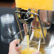 A hand pouring orange juice from a Tablecraft dual bowl dispenser into a glass.