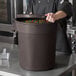 A man in a chef's uniform pouring a brown ingredient storage container full of candy.