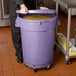A woman in a chef's uniform holding a large purple storage bin filled with food.