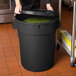 A woman holding a black round ingredient storage bin with green food inside.