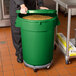 A man in a chef's uniform holding a large green mobile ingredient storage bin.