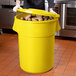 A man in a chef's uniform putting potatoes in a yellow round ingredient storage bin with a lid.