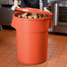 A man in a chef's uniform holding a large orange ingredient storage bin full of potatoes.