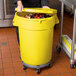 A woman using a yellow mobile ingredient storage bin in a school kitchen.