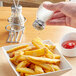 A person using a Tablecraft beehive salt shaker to pour salt on french fries.