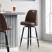 A Lancaster Table & Seating brown vinyl bar stool with a swivel bucket seat.