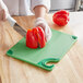 A person using a San Jamar green cutting board to cut a red bell pepper.
