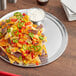 A wide rim aluminum pizza pan with a plate of nachos with sauce.