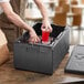 A man putting a red drink in a plastic cup holder on a Cambro black food pan carrier.