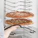 A person holding a pizza on a Choice aluminum pizza pan rack.