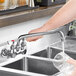 A person using a Waterloo wall-mounted faucet to pour water into a sink.