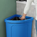 A person putting a clear plastic cup into a blue Lavex corner trash can lid.