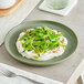 An Acopa Pangea sage matte porcelain plate with green beans and cream cheese on it.