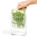 A hand holding a OXO GreenSaver clear plastic container with a green plant inside.