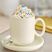 A fog white matte porcelain mug filled with hot chocolate topped with whipped cream and sprinkles.