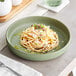 An Acopa Pangea sage matte porcelain pasta bowl filled with spaghetti and cheese.
