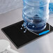 A white water jug and a blue water bottle with handles on a black Choice drain mat.