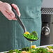 A person using an OXO nylon perforated spoon to serve broccoli and green peas.