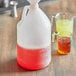 A translucent HDPE plastic jug with red liquid next to a measuring cup.