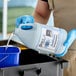 A person in blue gloves pouring Noble Chemical Actifoam cleaning solution from a white jug.