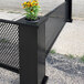 A black fence with a potted plant with yellow flowers in a SelectSpace corner planter.