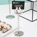 A Tablecraft stainless steel harp menu holder with a sign for mini cannoli on a plate of pastries.
