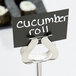 A sign that says "cucumber roll" in a Tablecraft stainless steel harp menu holder on a table in an Asian cuisine restaurant.